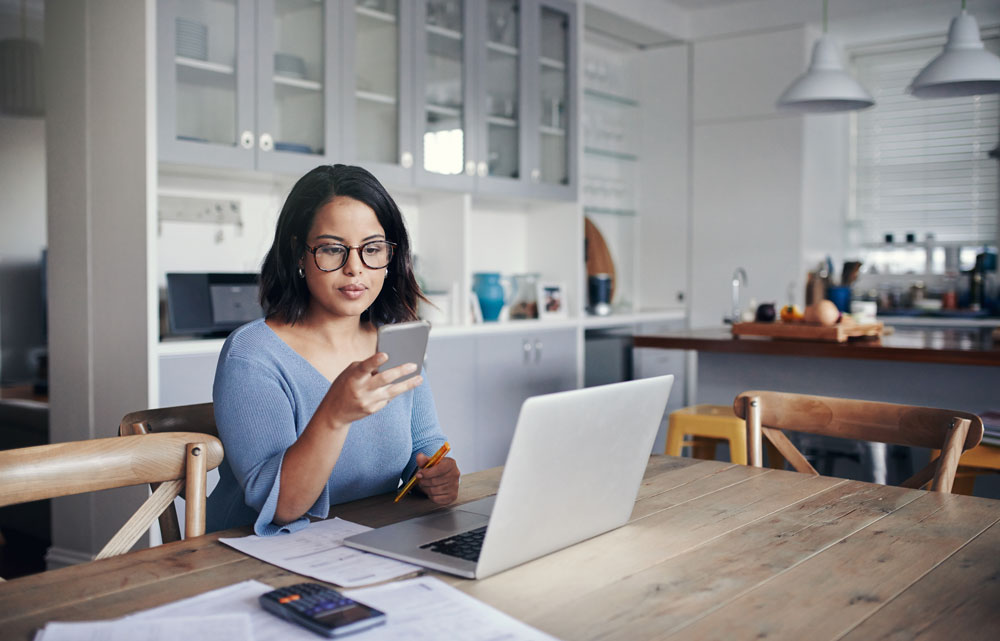 woman sitting at kitchen table looking at computer and phone