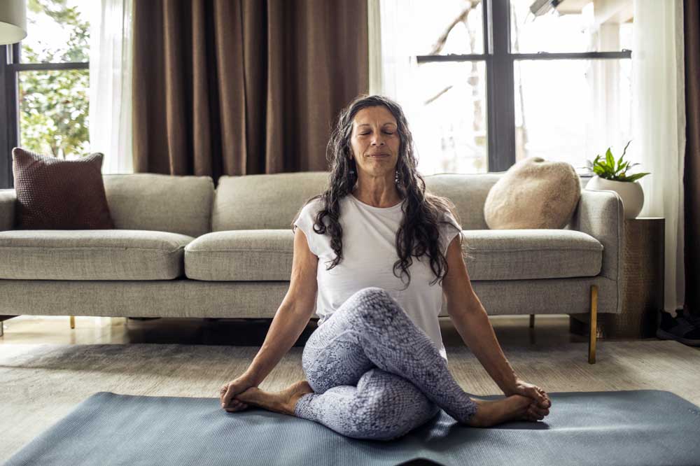 woman sitting crosslegg on yoga mat in room