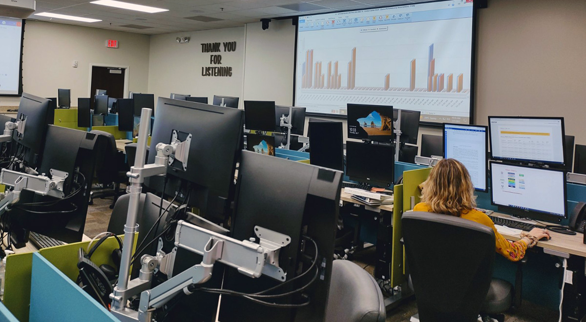 A person sits in front of a computer at a call center. The words Thank you for listening appear on the wall in bold black letters.