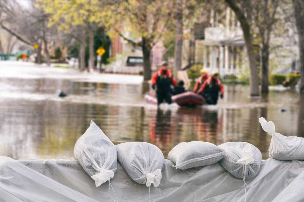Sandbags block flooded street with boat and rescue workers in background