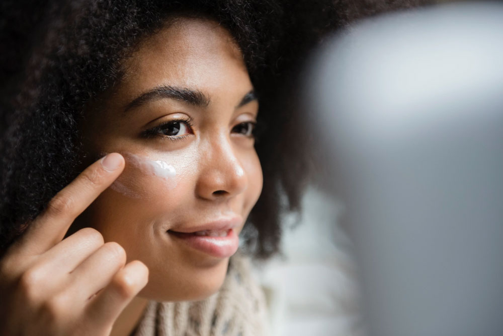 woman applying lotion around eyes in mirror