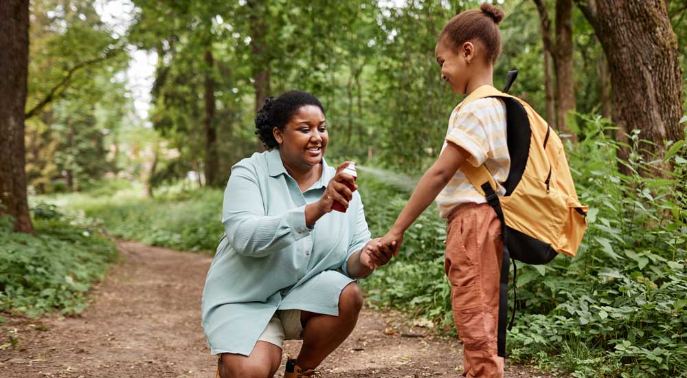 mother spraying child arms with bug spray in nature