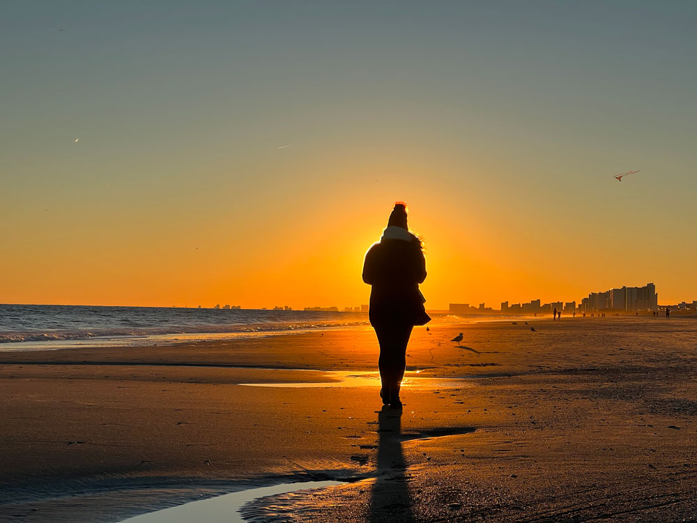 shadow of person walking into sunset on beach