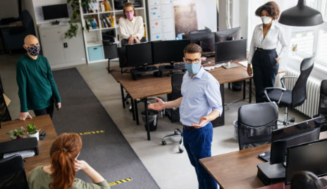 man addresses employees in office wearing masks