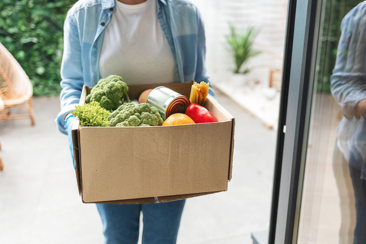 A person carries a box of fresh produce through a doorway