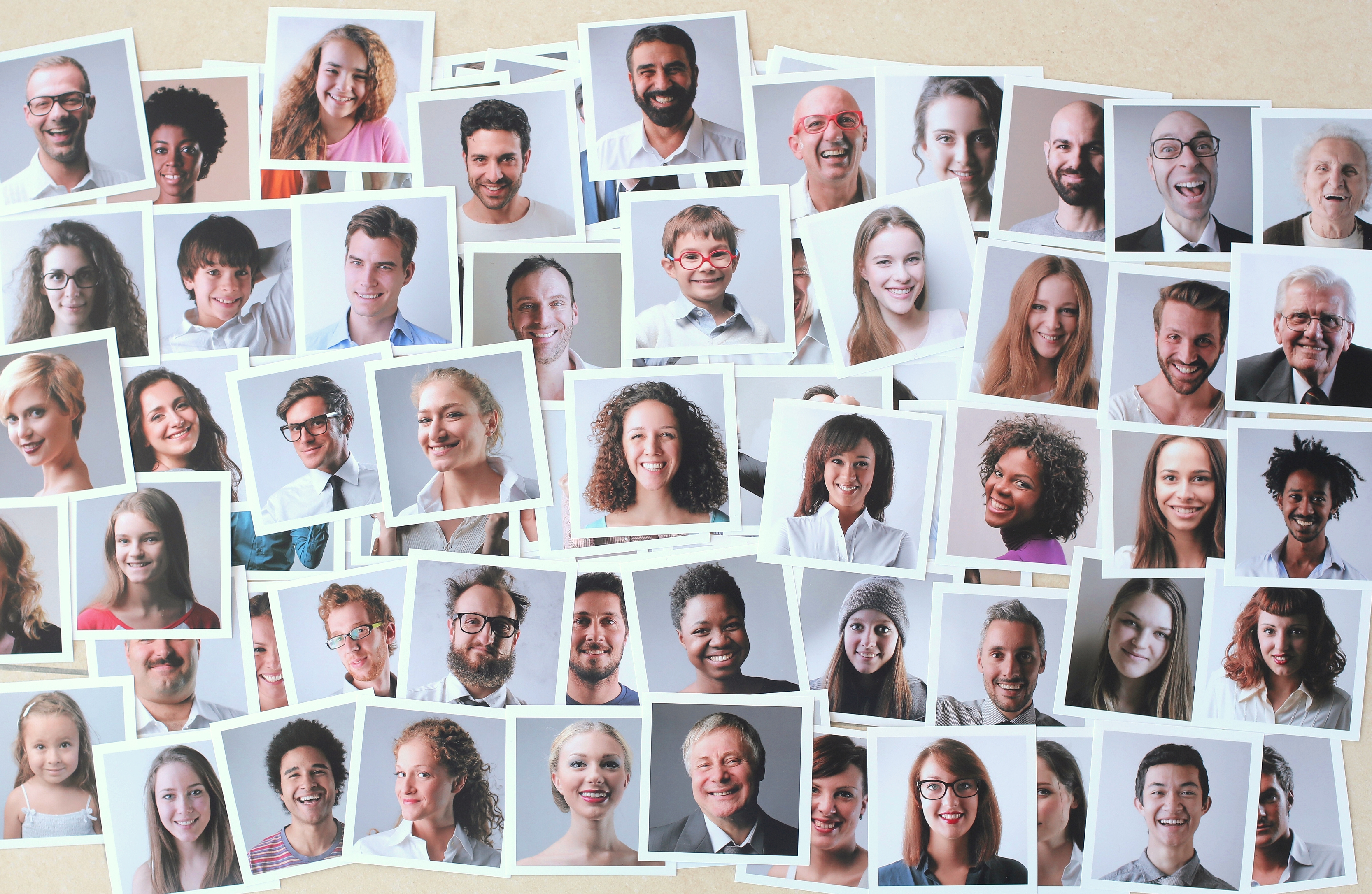 Snapshots of people of different races, genders and ages are scattered across a surface.