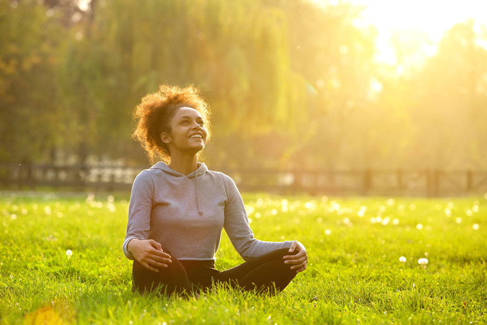 woman sitting cross legged in grass with sun in back