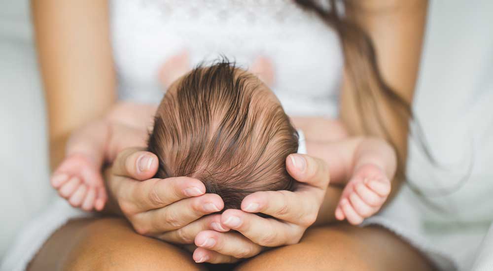 woman's hands holding newborn baby head