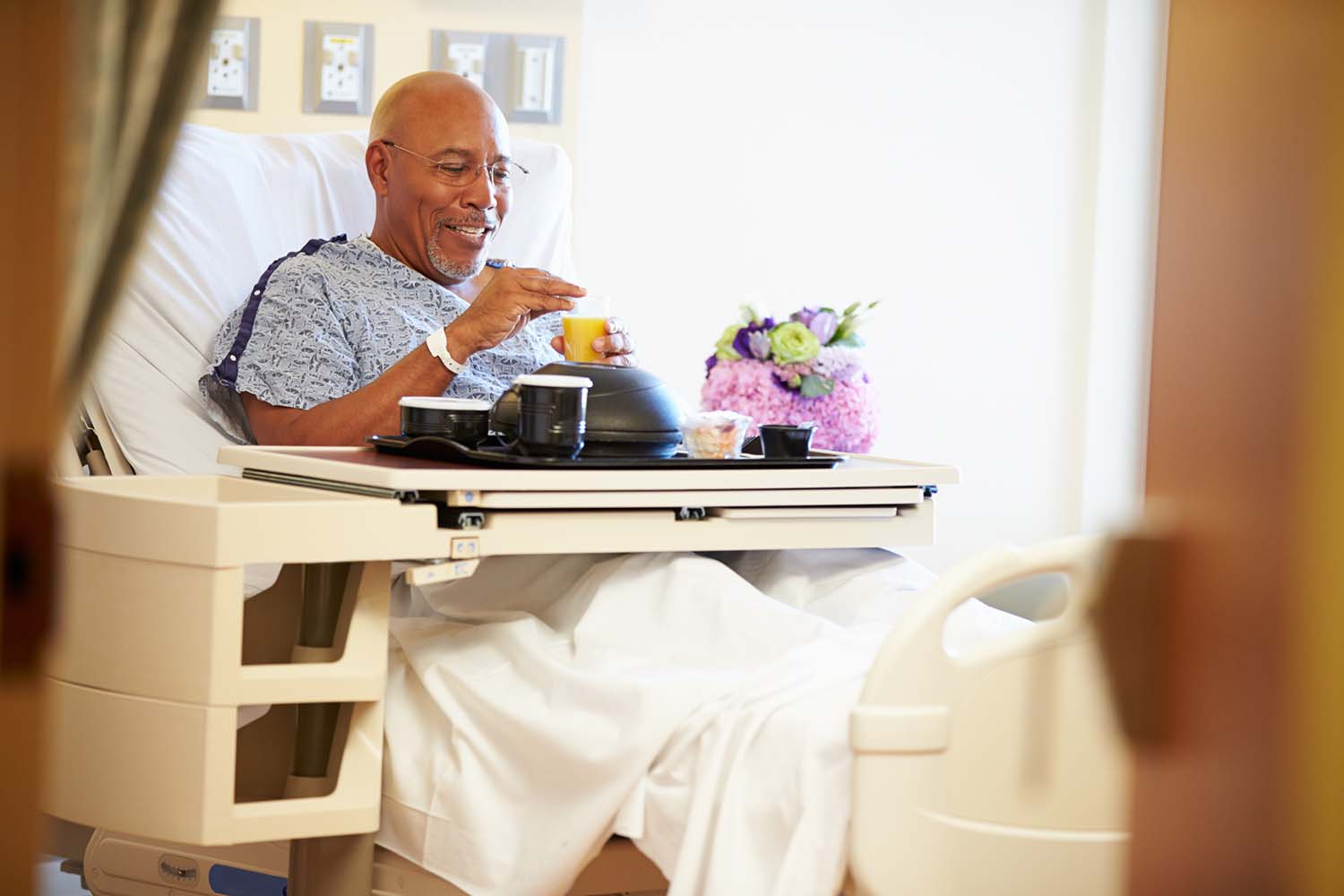 A man sits up in a hospital bed with a tray of food across his lap.