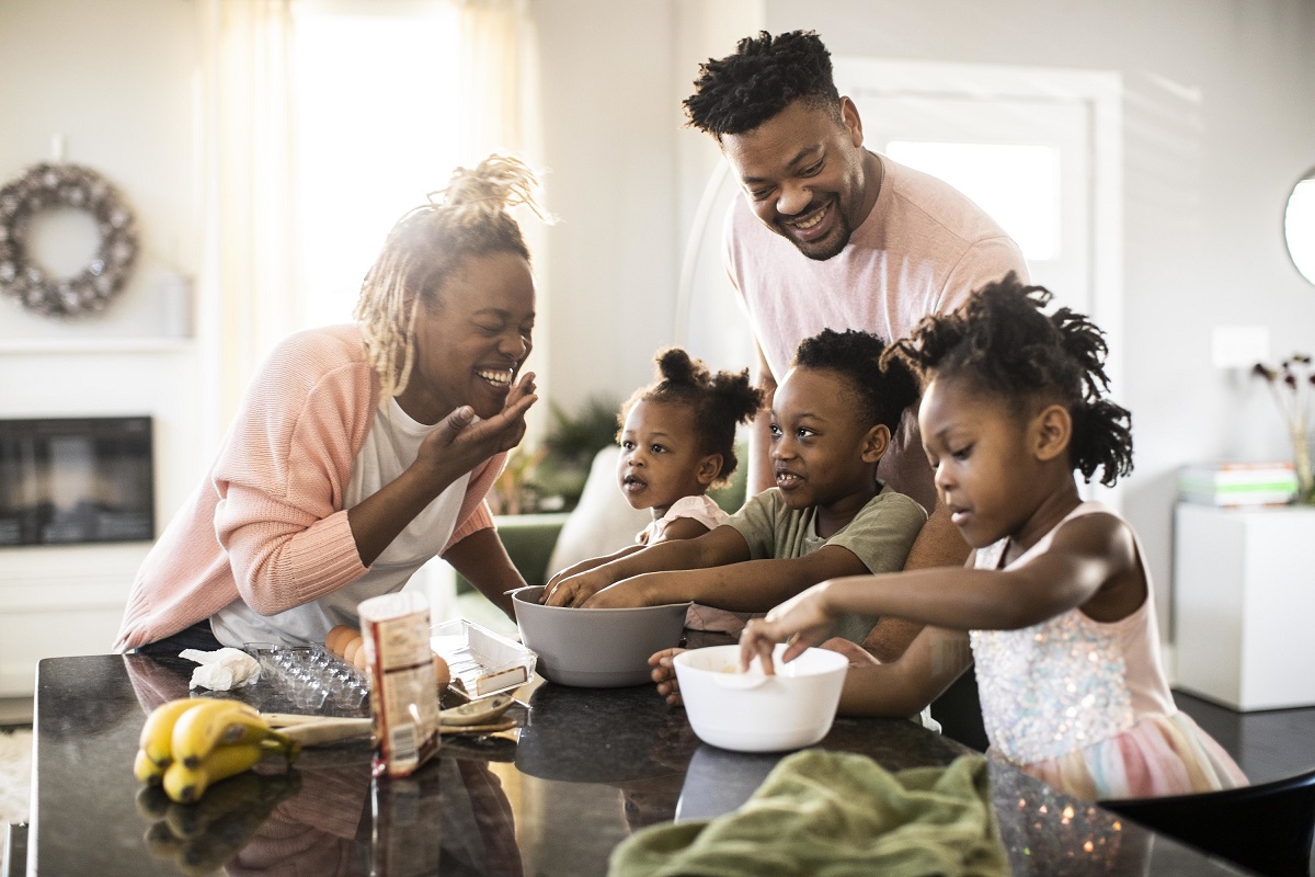 A mother, father and three young children make a meal together in their kitchen.