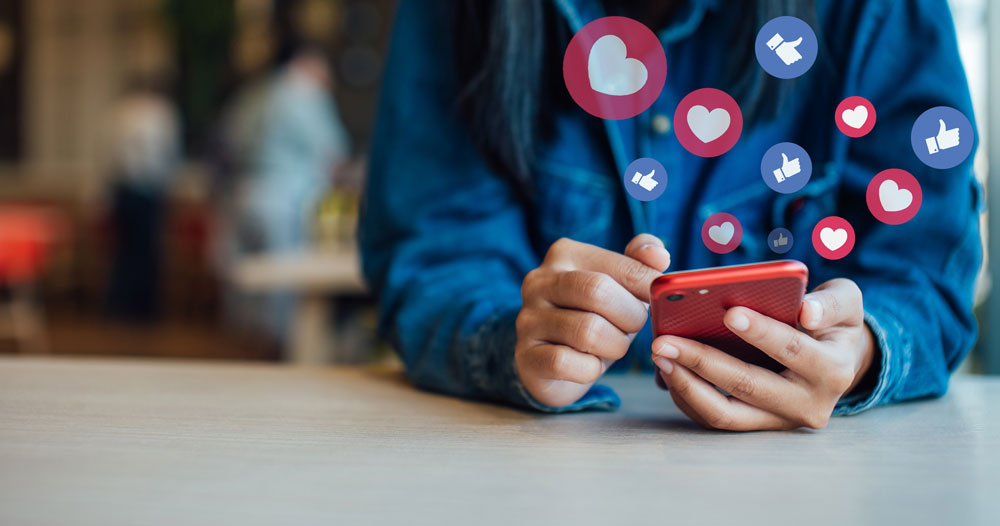 A person holds a smartphone as illustrations of hearts and likes float from the screen.