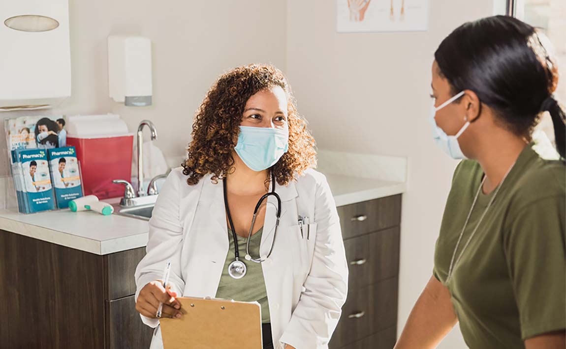 A doctor wearing a face mask speaks with a female patient wearing a face mask.