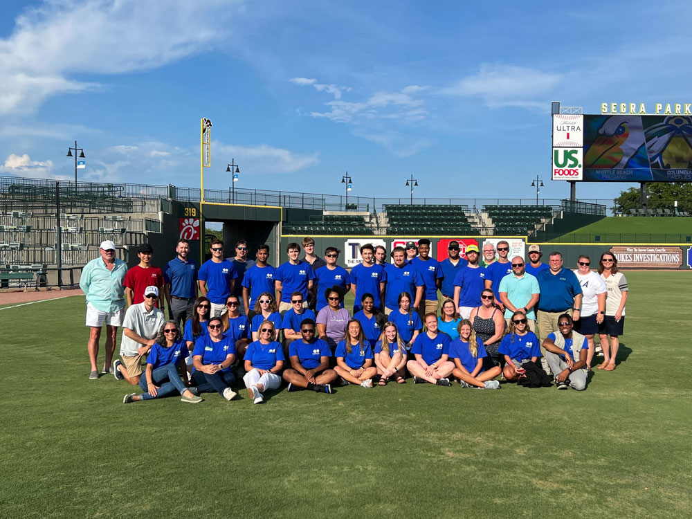 A group of interns sits on the baseball field at Segra Park.