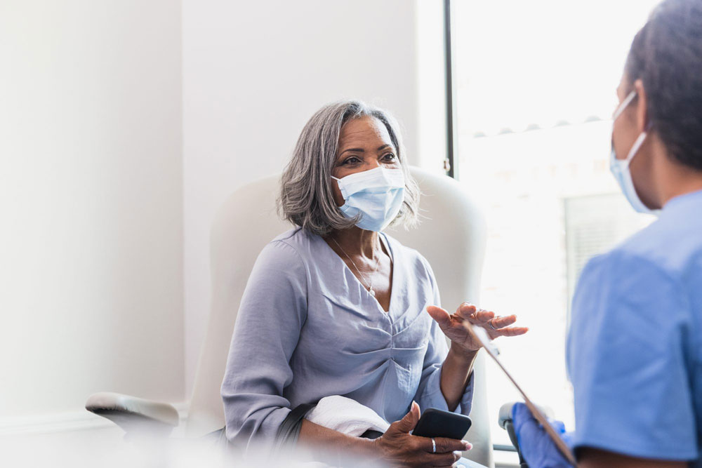 woman wearing mask talks with doctor in exam room